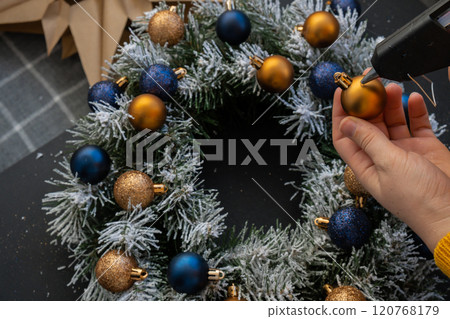 Crafter using hot glue Handmade Christmas wreath from festive blue and yellow decorations. Festive holiday preparation craft master class of creative making decor. Hands-on activities sustainable 120768179