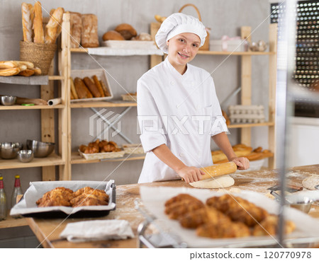 Adolescence girl baker works with rolling pin, rolls out and spreads out pieces of dough Adolescence girl baker works with rolling pin, rolls out and spreads out pieces of dough 120770978
