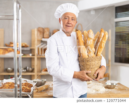 Bakery mature man employee holds basket of ready-made baguettes. Bakery mature man employee holds basket of ready-made baguettes. 120771044