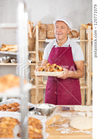 Elderly male baker with basket of croissants 120771079