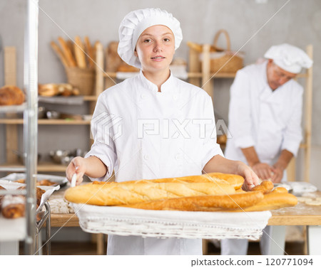 Portrait of female baker holding a basket of baguettes and fresh bread in hands Portrait of female baker holding a basket of baguettes and fresh bread in hands 120771094