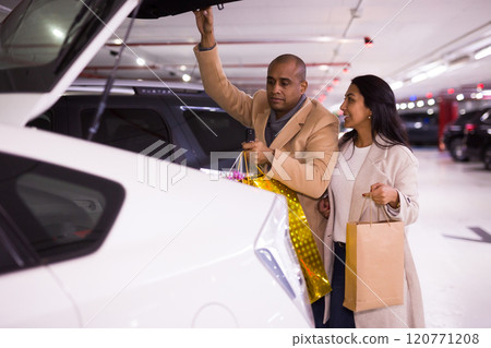 Married couple loading gift bags into trunk of car in an underground parking lot 120771208