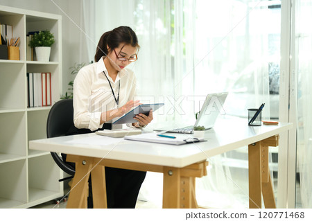 Young entrepreneur in glasses using digital tablet and working with document at desk Young entrepreneur in glasses using digital tablet and working with document at desk 120771468