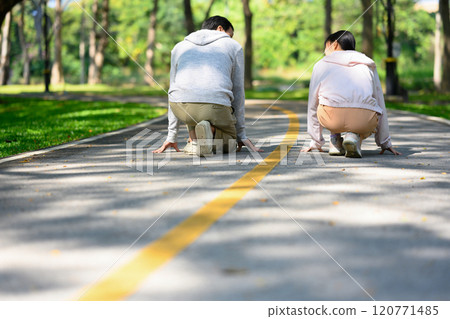 Senior man and young adult daughter crouching down in starting position on paved pathway in a park Senior man and young adult daughter crouching down in starting position on paved pathway in a park 120771485