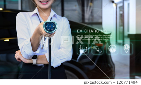 Smiling woman holding an EV charger with digital interface display to check real time data on the vehicle battery 120771494