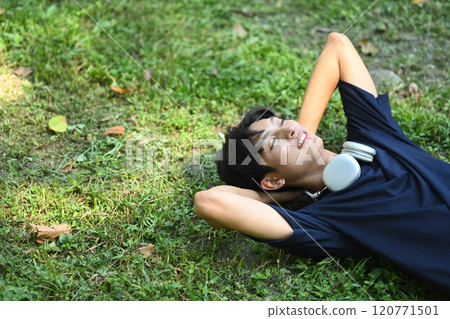 Young man relaxing after a jog lying down on the grass in park with warm sunlight 120771501