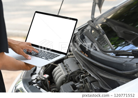 Mechanic using laptop to diagnose or research car issues in front of an open car hood Mechanic using laptop to diagnose or research car issues in front of an open car hood 120771552