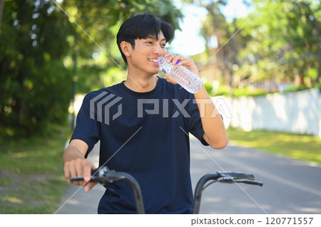 Smiling young man taking a break from riding bike and sipping water from a bottle 120771557
