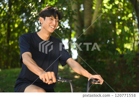 Cheerful young asian man riding bike through a serene park on sunny day 120771558