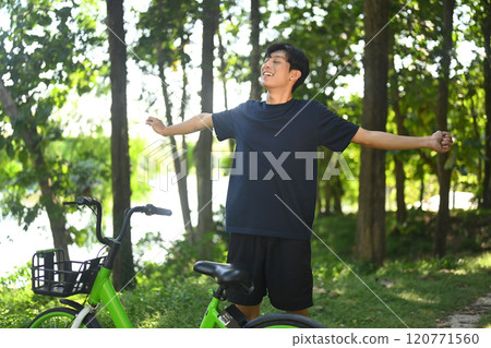 Carefree asian man standing with arms outstretched enjoying the fresh air outdoors after a bike ride Carefree asian man standing with arms outstretched enjoying the fresh air outdoors after a bike ride 120771560