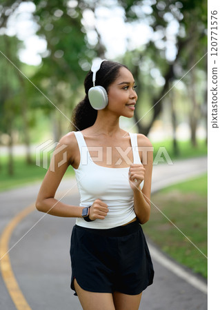 Portrait of smiling African American woman wearing headphone jogging along a scenic park Portrait of smiling African American woman wearing headphone jogging along a scenic park 120771576