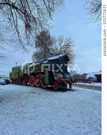 Poland, Przeworsk. December 2023. Old steam locomotive in the yard of a country house in winter standing as museum exposition Poland, Przeworsk. December 2023. Old steam locomotive in the yard of a country house in winter standing as museum exposition 120771611