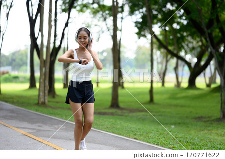 Smiling young woman checking her fitness data on smartwatch while jogging in a park 120771622