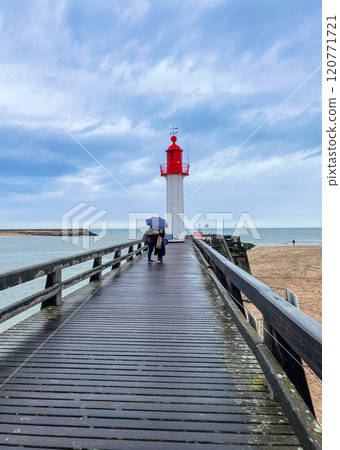 Red lighthouse with wooden pier with blue sky with rainy clouds background in the Normandy, France.  120771721