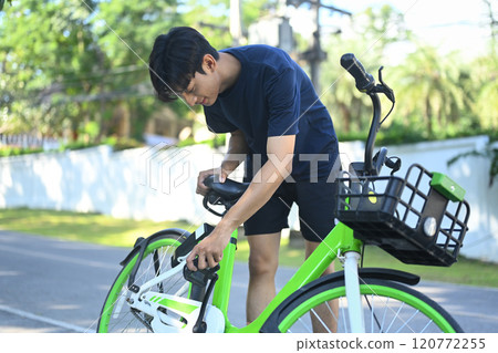 Young asian man inspecting his bicycle in a park preparing for a bike ride. 120772255