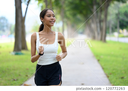 Delighted young African woman jogging along a peaceful park path on beautiful day 120772263