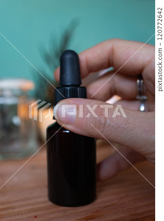 Woman's hand holding a bottle of essential oil.Blurred background 120772642