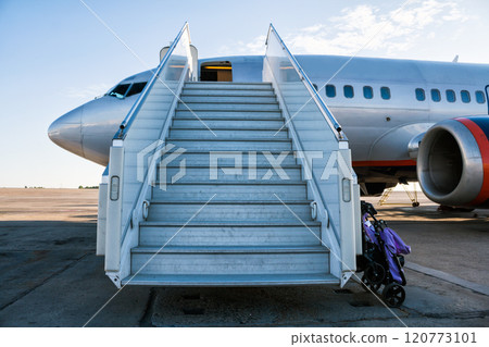 Airplane with a passenger boarding steps on the airport apron with a stroller prepared for the carriage of children Airplane with a passenger boarding steps on the airport apron with a stroller prepared for the carriage of children 120773101