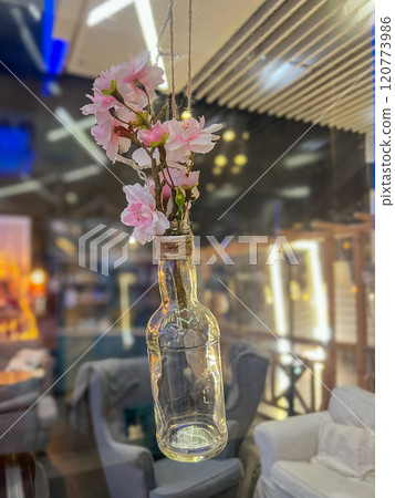 Vintage glass bottle with bouquet of cherry blossoms in a glass vase in a cafe hanging in the air 120773986