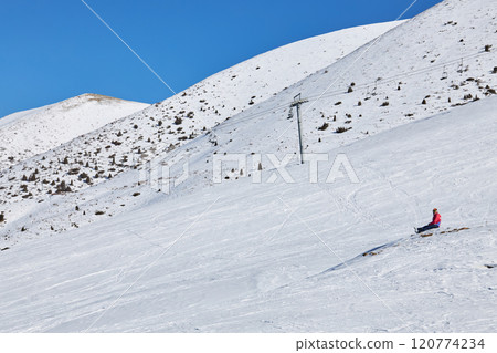 Man in red jacket relaxing sitting on mountainside at ski resort 120774234