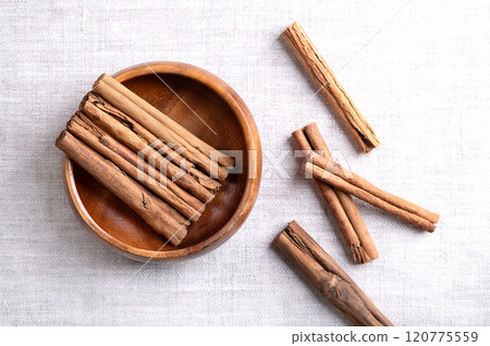 Ceylon cinnamon sticks in a wooden bowl on linen fabric. Parallel arranged whole, dried bark strips of Cinnamomum verum, used mainly as an aromatic condiment and as a flavouring additive. Food photo. Ceylon cinnamon sticks in a wooden bowl on linen fabric. Parallel arranged whole, dried bark strips of Cinnamomum verum, used mainly as an aromatic condiment and as a flavouring additive. Food photo. 120775559