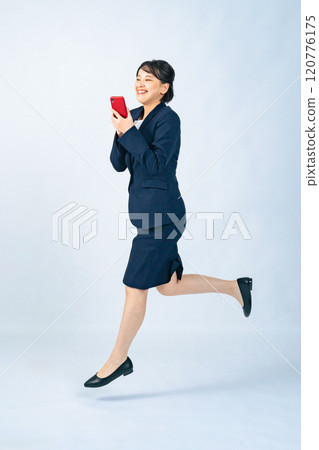一名身穿西裝的女子看著智慧型手機跳躍的全身照片 一名身穿西裝的女子看著智慧型手機跳躍的全身照片 120776175