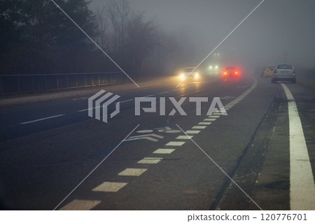 Car traveling on the foggy road with headlights or headlamps on. Low visibility - Dangerous driving of cars in winter in bad weather. 120776701