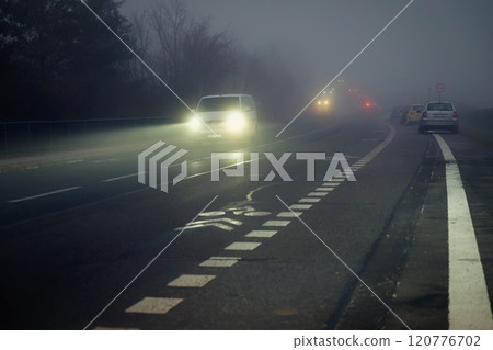 Bright headlights of a car driving on foggy winter road 120776702