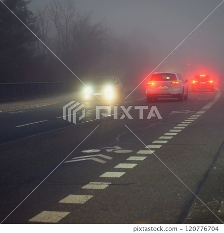 Bright headlights of a car driving on foggy winter road 120776704
