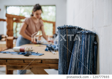Young businesswoman working on workbench, preparing old fabric for weaving. Upcycled textile, small weaving business and circular economy. 120777693