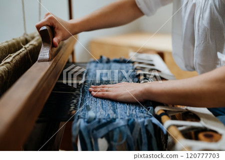 Close up of woman working on wooden loom, weaving a rug from old fabrics. Upcycling in business and circular economy. Close up of woman working on wooden loom, weaving a rug from old fabrics. Upcycling in business and circular economy. 120777703