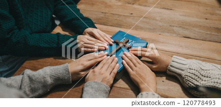 Group of Christians sit together and pray around a wooden table with blurred open Bible pages in their homeroom. Prayer for brothers, faith, hope, 120778493
