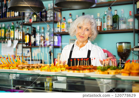 Elderly female bartender offering delectable sandwiches pinchos 120778629