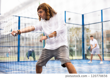 Male players playing padel in a padel court outdoor behind net Male players playing padel in a padel court outdoor behind net 120778656