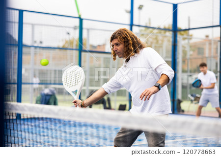 Concentrated man playing padel tennis on open court 120778663