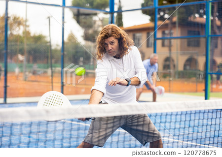 Focused adult man playing paddle tennis outdoors Focused adult man playing paddle tennis outdoors 120778675