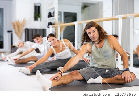 Middle-aged man practicing pilates on gray mat in gym room 120778689