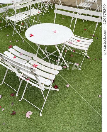 White folding tables and chairs in fall at the park cafe. Red maple fallen leaves. Nature and recreation. Garden furniture on green lawn. View from above.  120779240