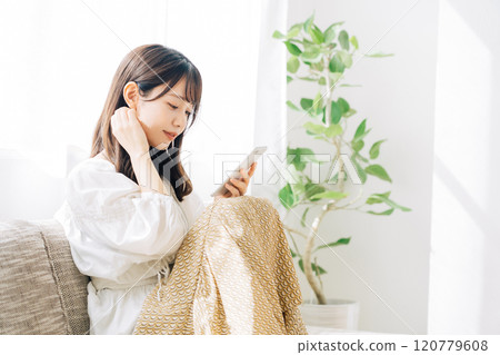 Woman sitting on a sofa and looking at a smartphone 120779608