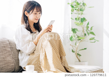 Woman sitting on a sofa and looking at a smartphone Woman sitting on a sofa and looking at a smartphone 120779611