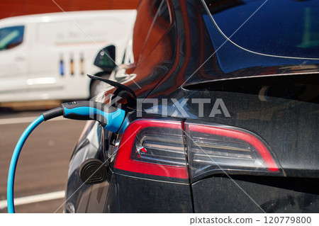 Close up of electric vehicle charging on public station at city street. EV car with plugged in cable recharging battery. Sustainable and eco-friendly transportation 120779800
