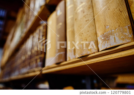 Row of aged leather-bound books on wooden shelf in library Row of aged leather-bound books on wooden shelf in library 120779801