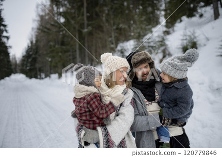 Rear view of family is enjoying winter holiday in the mountains, holding hands while walking through the snowy forest. Rear view of family is enjoying winter holiday in the mountains, holding hands while walking through the snowy forest. 120779846