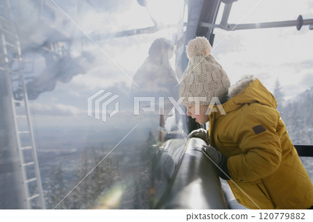 Little boy riding cable car to the top of the mountain during winter holiday with his family. Little boy riding cable car to the top of the mountain during winter holiday with his family. 120779882