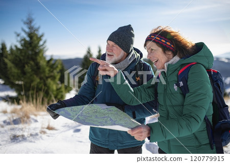 Older tourist using map during their hike in snowy winter mountains. Elderly couple in winter nature. 120779915