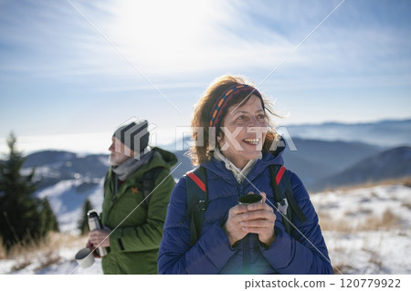 Active seniors resting, drinking warm tea from thermos. Romantic winter hike for an elderly couple in snowy mountains. Active seniors resting, drinking warm tea from thermos. Romantic winter hike for an elderly couple in snowy mountains. 120779922