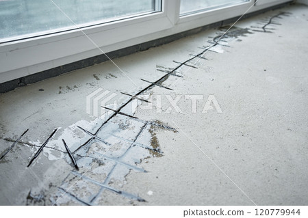 Repairing cracks in concrete floor near window using sealant. Renovation process in house under construction Repairing cracks in concrete floor near window using sealant. Renovation process in house under construction 120779944