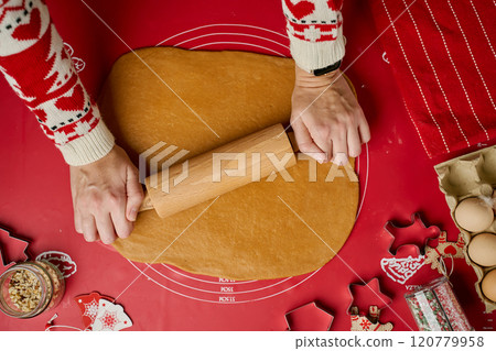 Woman in festive red sweater rolling dough for gingerbread cookies. Process of cooking traditional Christmas sweets for winter holidays at home kitchen Woman in festive red sweater rolling dough for gingerbread cookies. Process of cooking traditional Christmas sweets for winter holidays at home kitchen 120779958