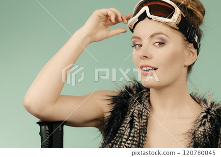 Woman holding ski goggles and poles 120780045