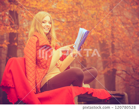 Blonde girl reading book in autumn scenery 120780528